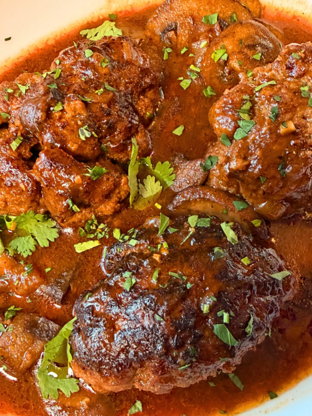 Salisbury steak in a pool of mushroom gravy on a white serving plate.