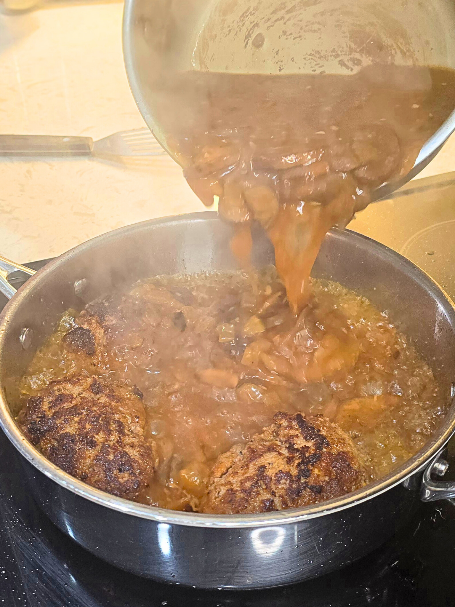 Pouring mushroom gravy into a pan of Salisbury steak.