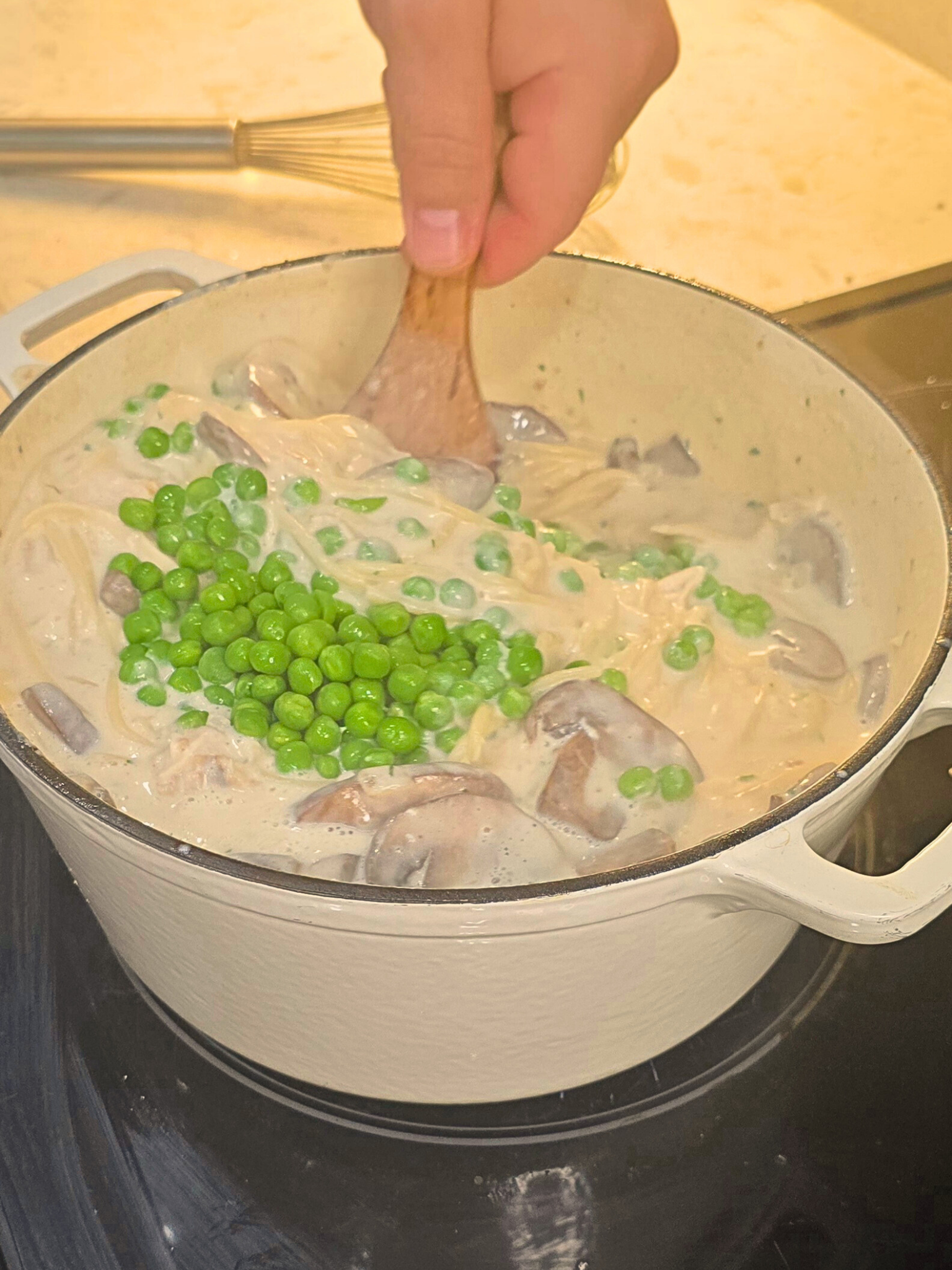 Stirring frozen peas into a Dutch oven of turkey Tetrazzini.