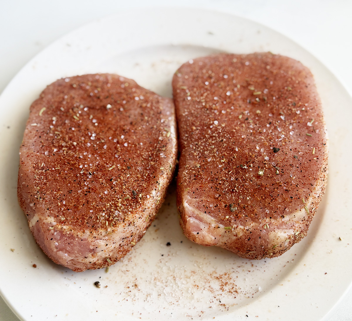 Two boneless pork chops with seasoning ready to be breaded and made in an air fryer.