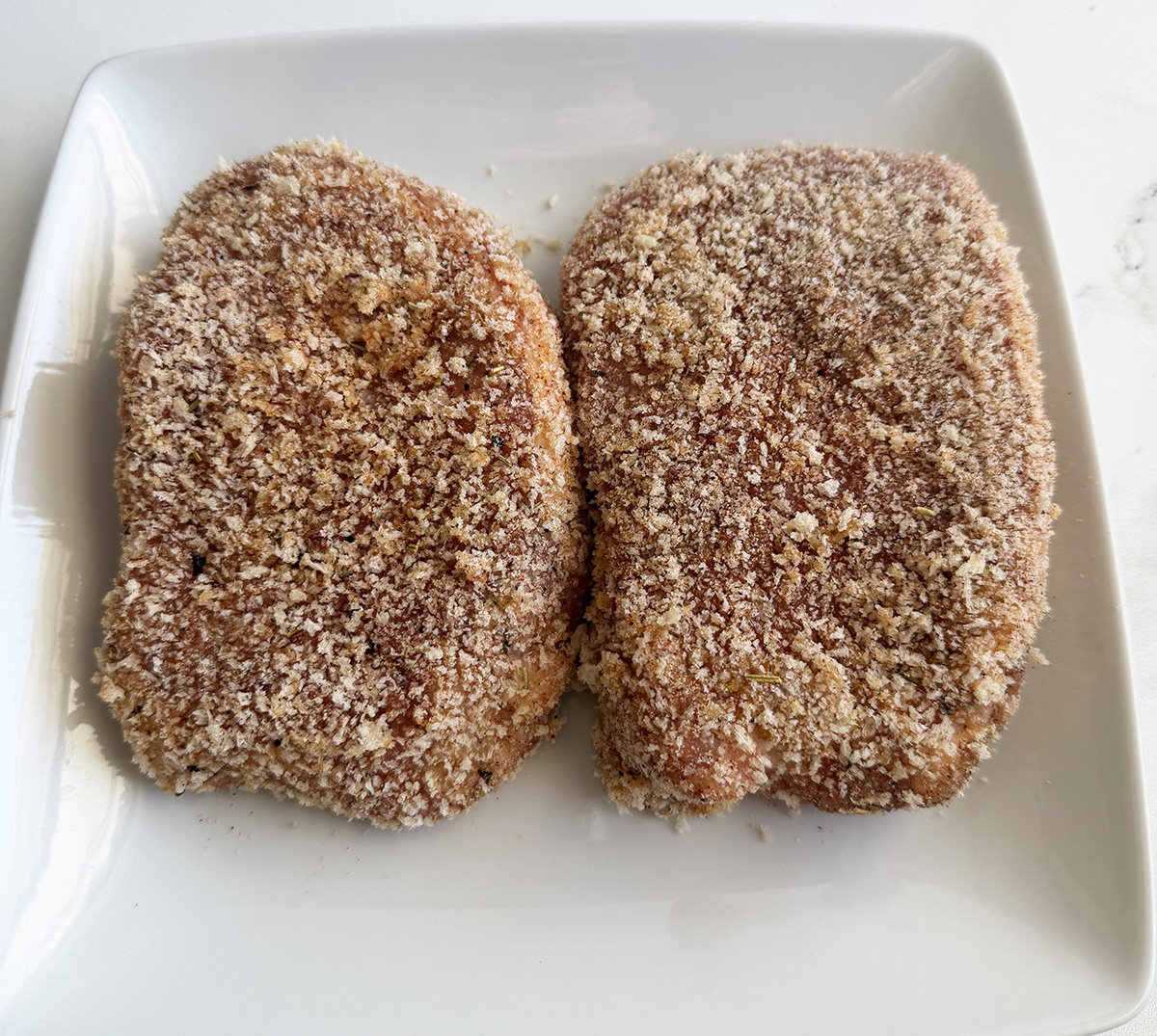 Two boneless pork chops seasoned and breaded and ready for the air fryer.