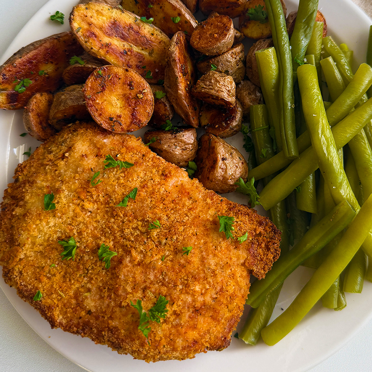 Breaded air fryer pork chops served with roasted potatoes and green beans.
