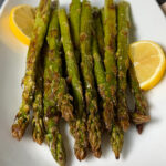 Perfectly oven roasted asparagus served on a plater with lemon wedges.