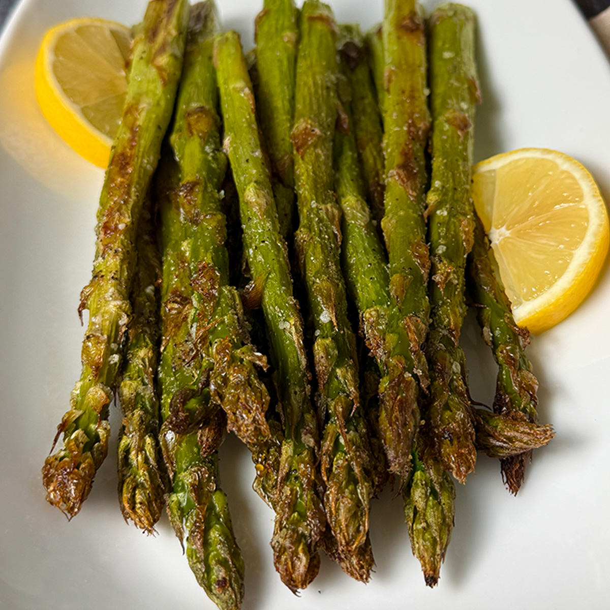Perfectly oven roasted asparagus served on a plater with lemon wedges.