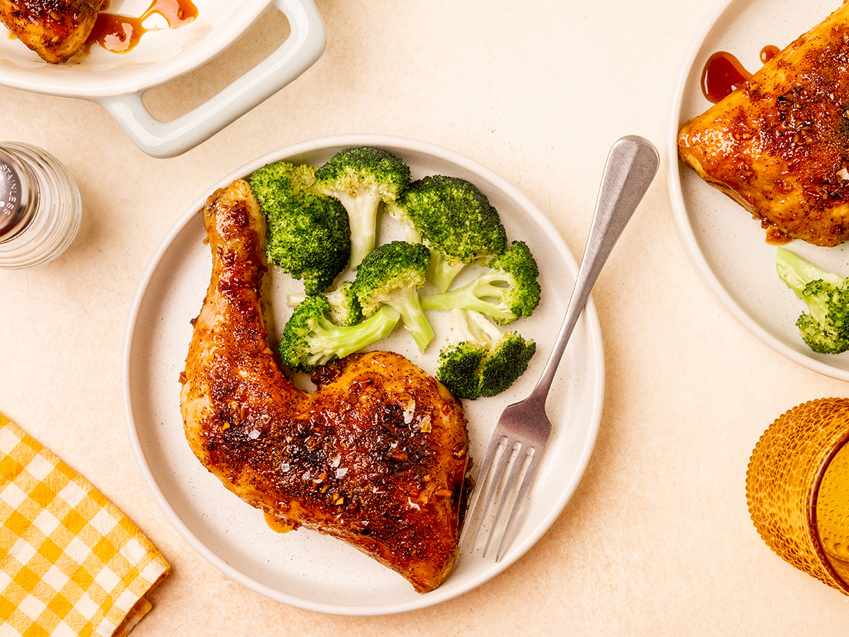 Honey garlic chicken quarters served on a white dinner plate with broccoli.